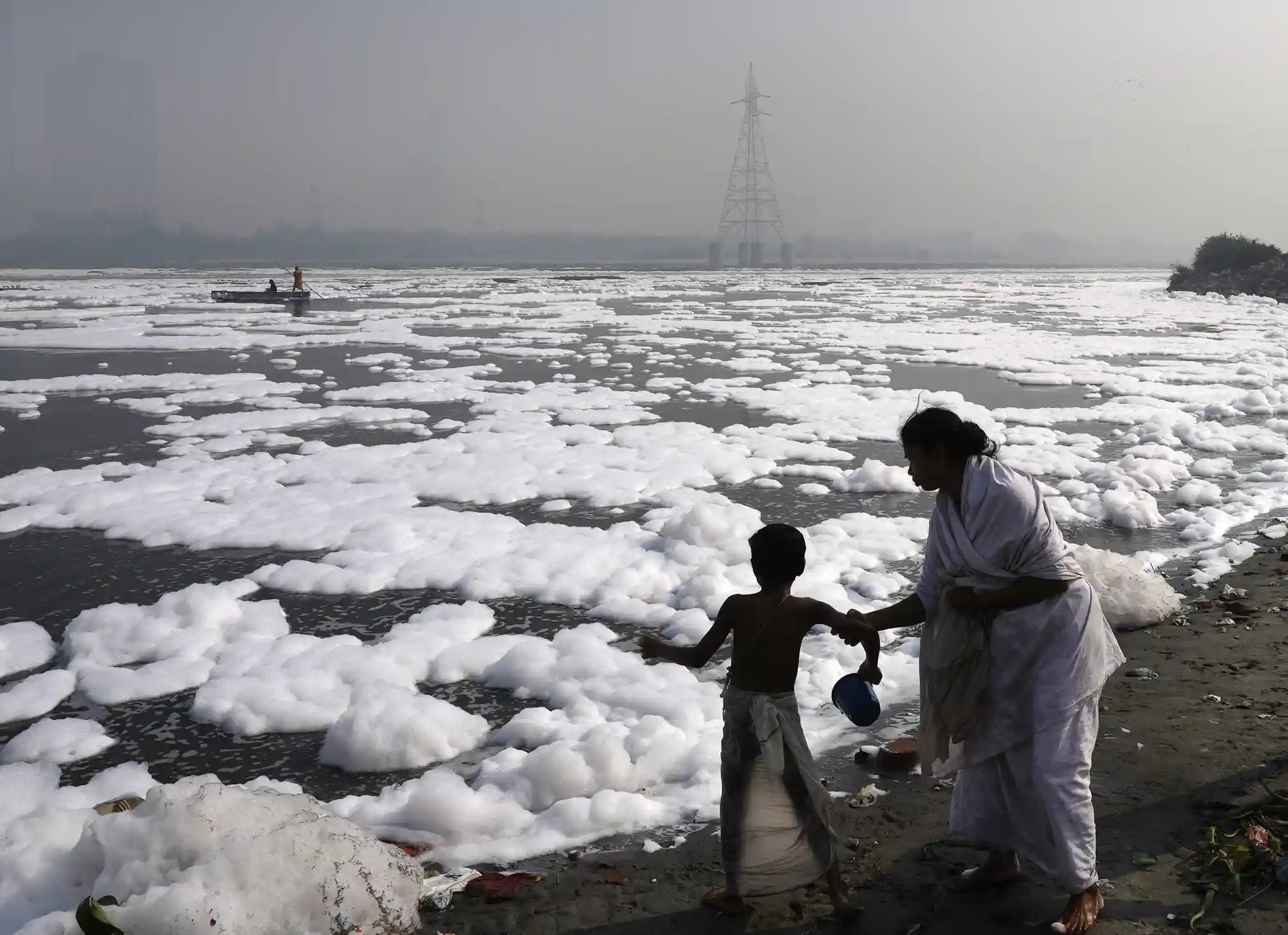 A girl stops her son going into the Yamuna River, covered by a chemical foam